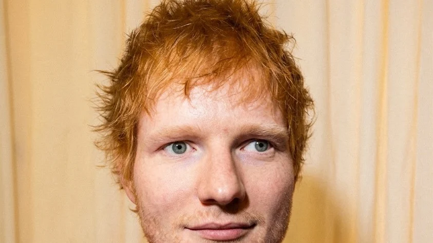 Ed Sheeran in a pink hoodie with "PLAY" written on it.