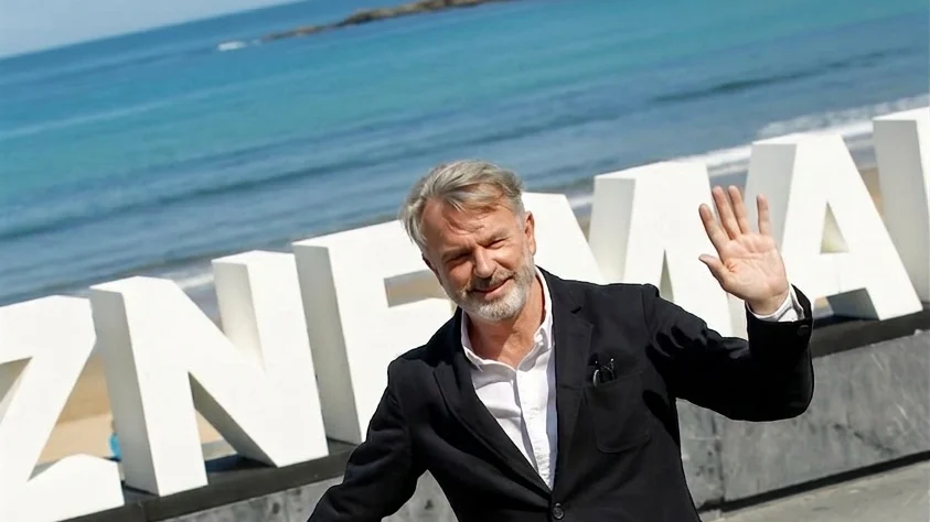 Sam Neill smiling and waving at the 67th San Sebastian Film Festival.