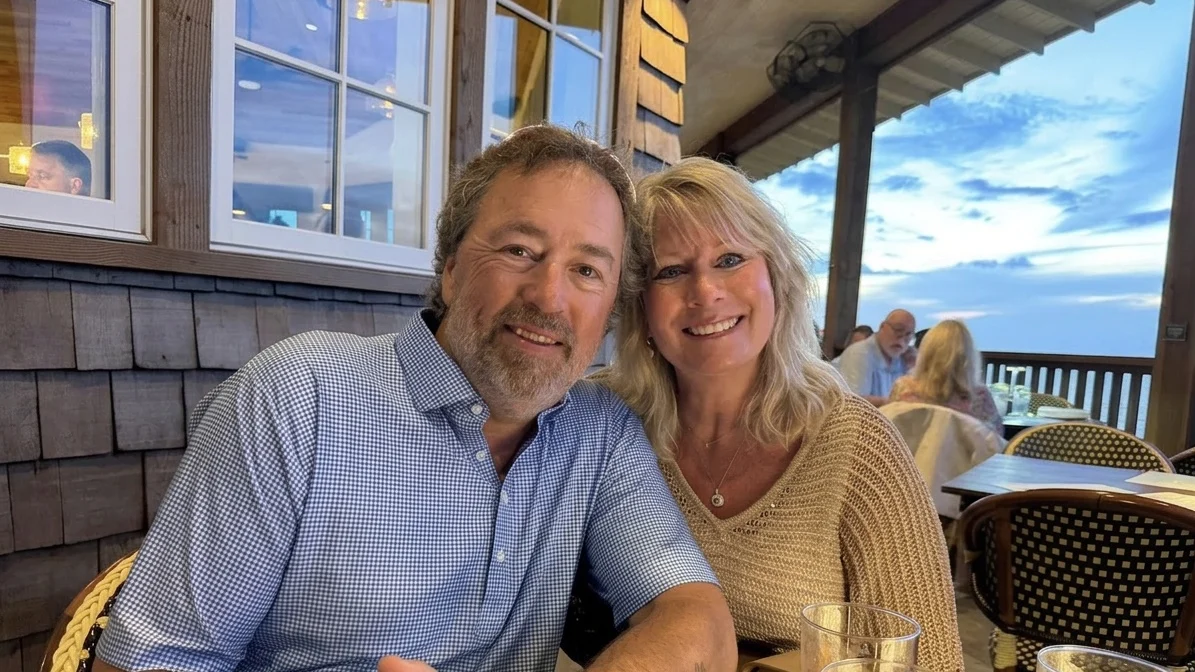 Lisa and Al Robertson smiling while seated at an outdoor restaurant.