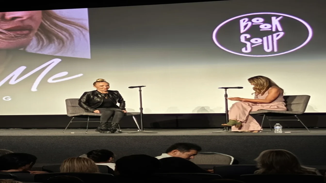 Hayden Panettiere speaking at an event, dressed in a black leather jacket and jeans, sitting next to another woman on a stage.