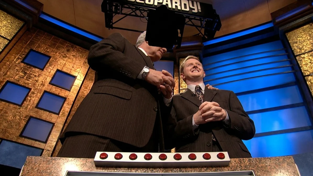 Alex Trebek and Ken Jennings smiling on the Jeopardy set, with winnings of $1,004,960 displayed on a monitor.