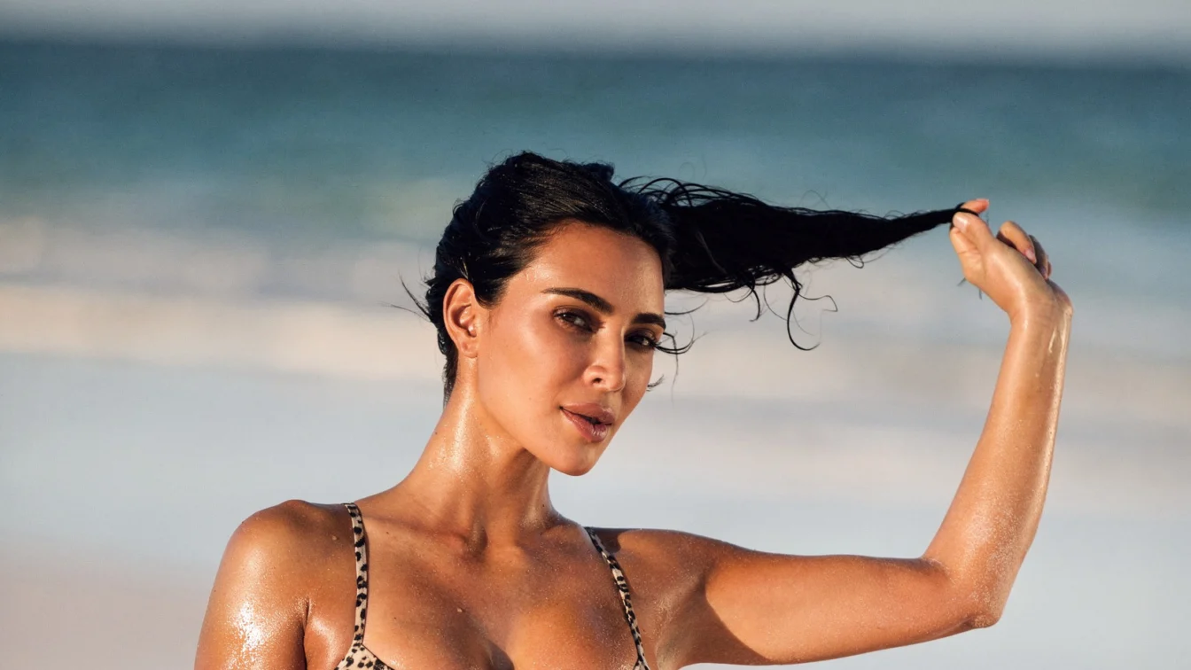 Kim Kardashian in a leopard print bikini, posing with wet hair on a beach.