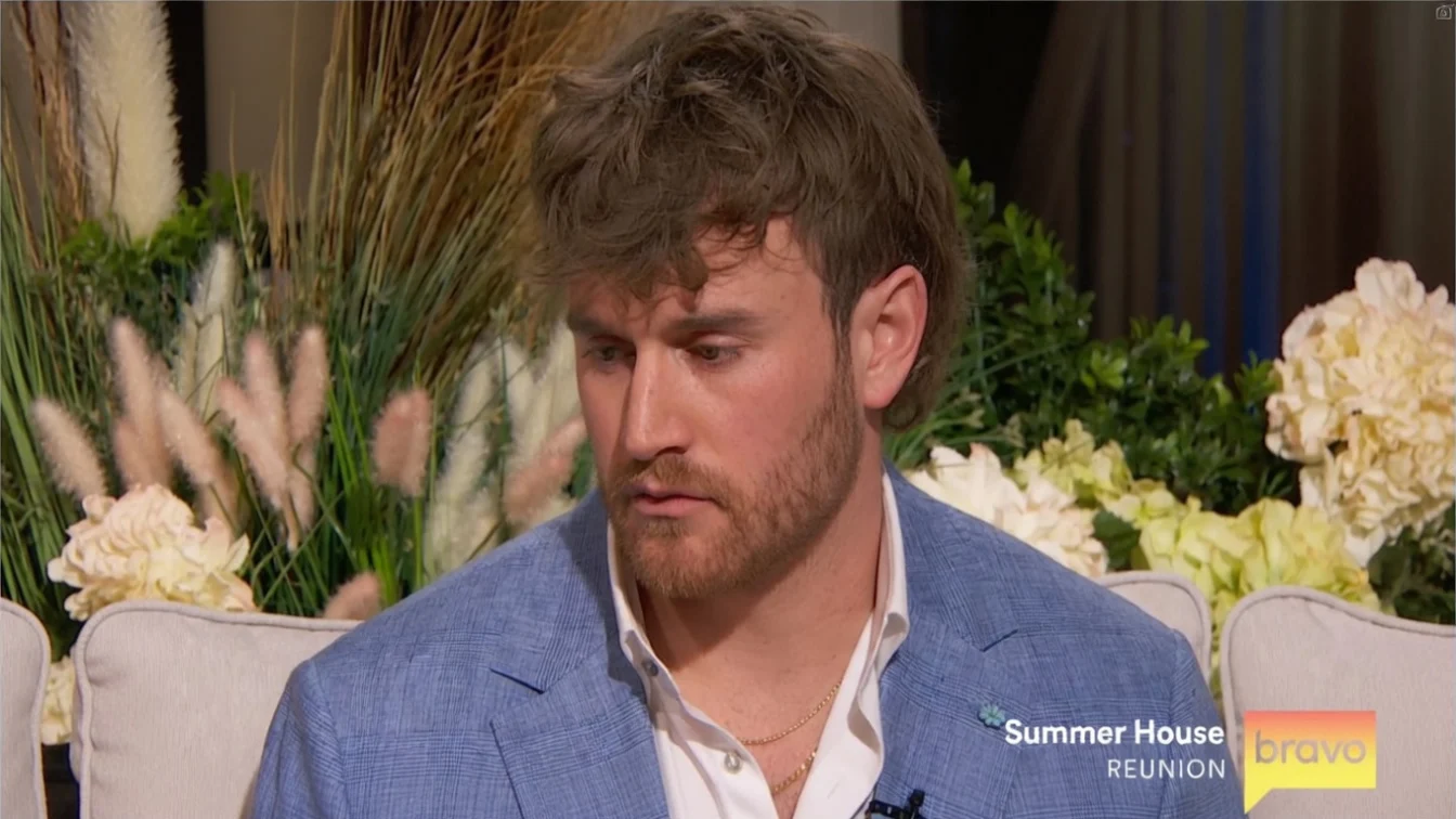 West Wilson, a man with brown hair and a beard, in a blue blazer and white shirt, looks down during the "Summer House" reunion.