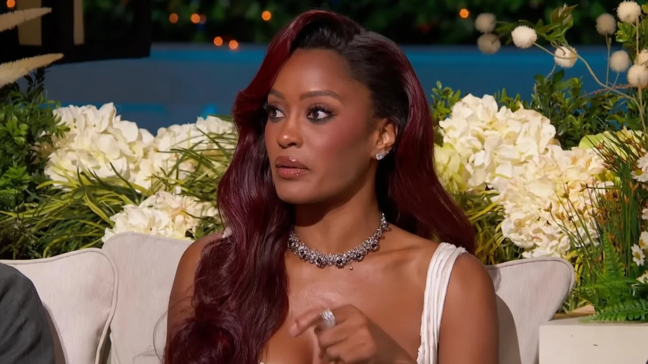 Ciara Miller speaking, looking concerned, with dark red hair and a statement necklace.