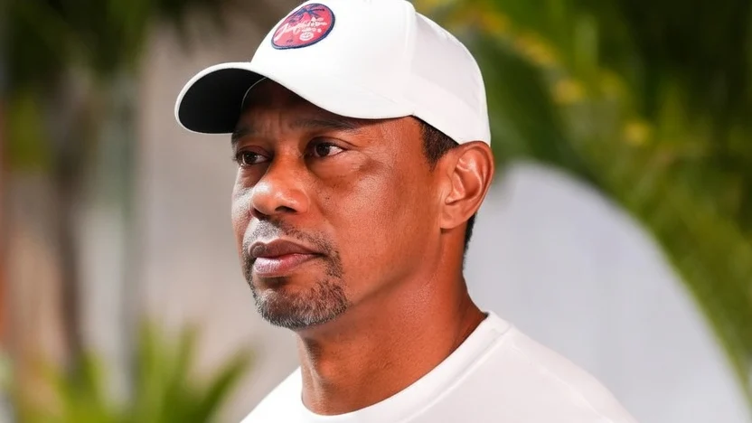 Tiger Woods in a white long-sleeved shirt and white cap, with "Jupiter Links GC" visible on the cap.